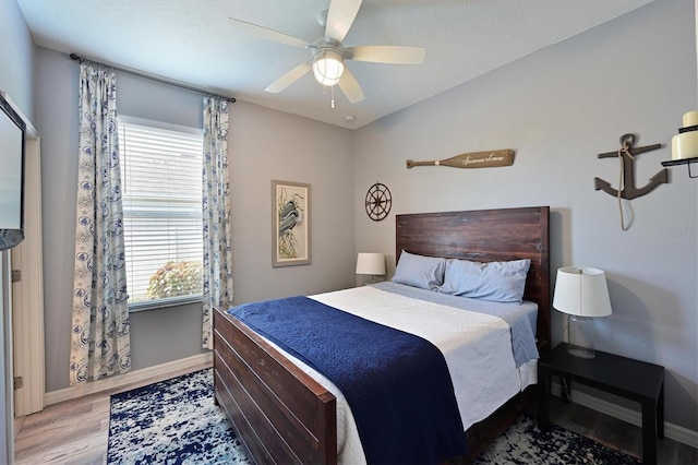 bedroom featuring ceiling fan, baseboards, multiple windows, and wood finished floors