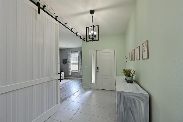 foyer with a barn door, baseboards, a notable chandelier, and light tile patterned floors