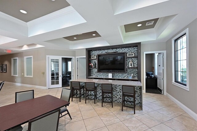 interior space featuring french doors, a raised ceiling, a kitchen bar, crown molding, and light tile patterned flooring