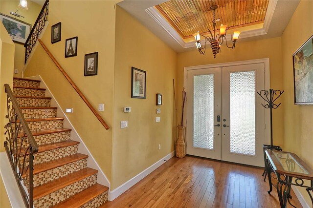 foyer entrance featuring light hardwood / wood-style floors, wooden ceiling, a tray ceiling, french doors, and a chandelier