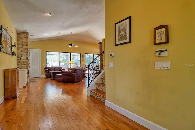 hall featuring vaulted ceiling, light hardwood / wood-style floors, and a textured ceiling