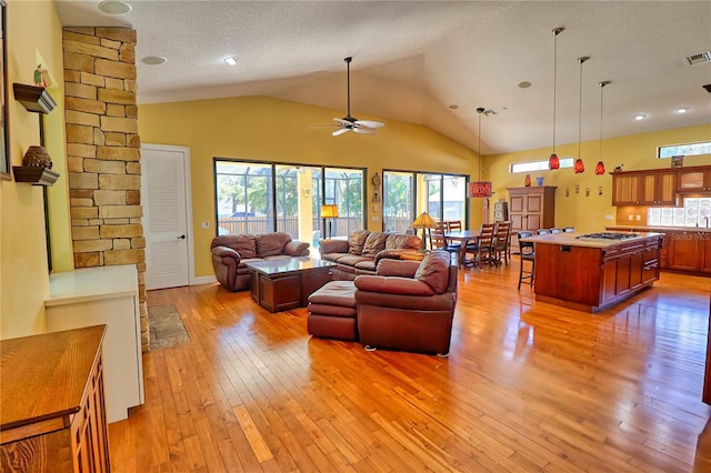 living room with light wood-type flooring, a textured ceiling, lofted ceiling, and ceiling fan