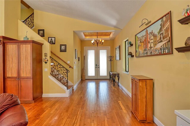 entrance foyer featuring french doors, vaulted ceiling, light wood-type flooring, and a chandelier