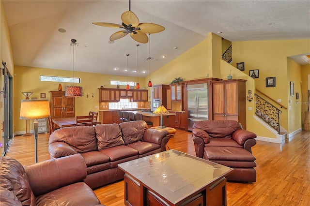 living room with ceiling fan, light wood-type flooring, and high vaulted ceiling