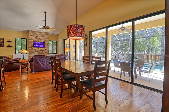 dining area featuring ceiling fan, a stone fireplace, lofted ceiling, and hardwood / wood-style floors