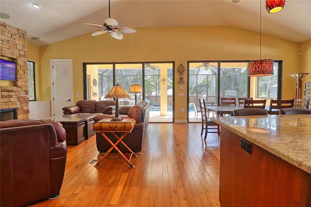 living room with ceiling fan, a fireplace, vaulted ceiling, and light hardwood / wood-style flooring