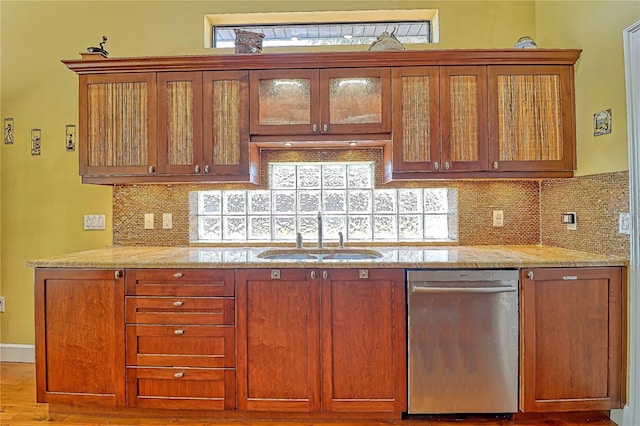 kitchen with light stone counters, sink, stainless steel dishwasher, light hardwood / wood-style flooring, and backsplash