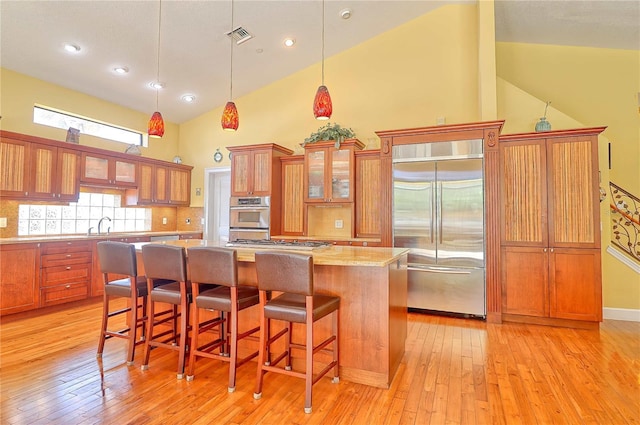 kitchen with pendant lighting, a kitchen island, high vaulted ceiling, light hardwood / wood-style flooring, and appliances with stainless steel finishes