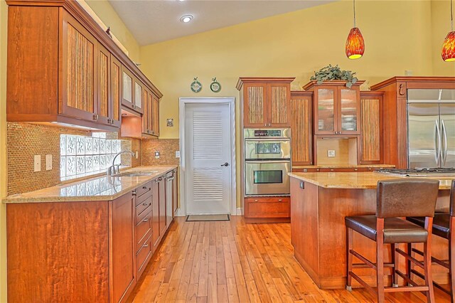 kitchen with light wood-type flooring, light stone counters, sink, hanging light fixtures, and appliances with stainless steel finishes