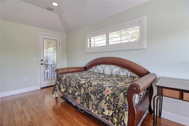 bedroom with a textured ceiling, lofted ceiling, and hardwood / wood-style flooring