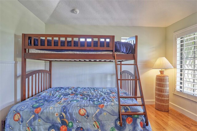 bedroom with a textured ceiling, lofted ceiling, and hardwood / wood-style floors