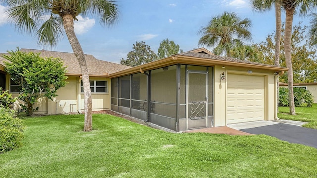 exterior space featuring a sunroom, a garage, and a lawn