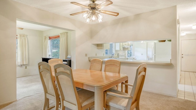 dining space with a textured ceiling, light carpet, and ceiling fan