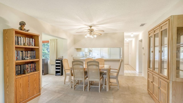 dining space featuring a textured ceiling, ceiling fan, and light colored carpet