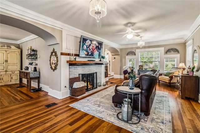 living room featuring wood-type flooring, ceiling fan with notable chandelier, a fireplace, and ornamental molding