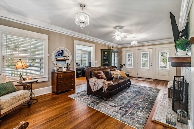 living room featuring crown molding, wood-type flooring, a fireplace, and ceiling fan with notable chandelier