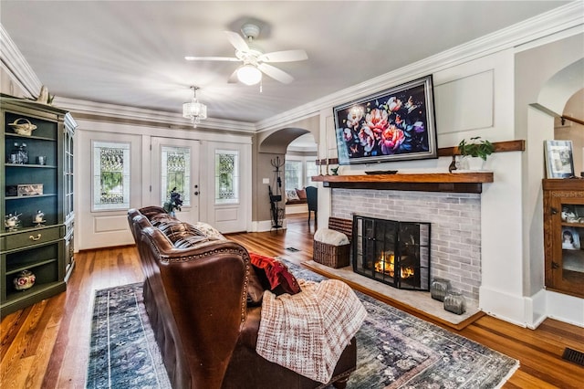 living room with wood-type flooring, ornamental molding, ceiling fan, and a brick fireplace