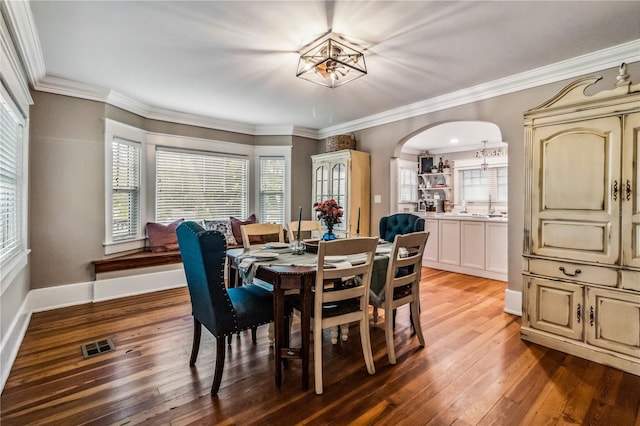 dining area with a notable chandelier, wood-type flooring, sink, and crown molding