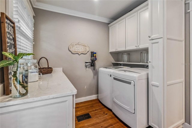 laundry area featuring washing machine and dryer, ornamental molding, dark hardwood / wood-style flooring, and cabinets