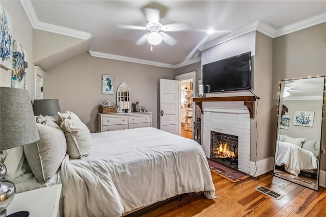 bedroom featuring light hardwood / wood-style floors, a fireplace, ceiling fan, and crown molding