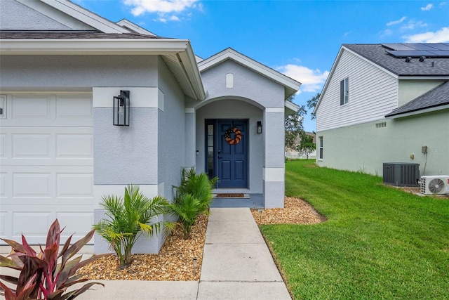 entrance to property with a garage, ac unit, a yard, and central AC