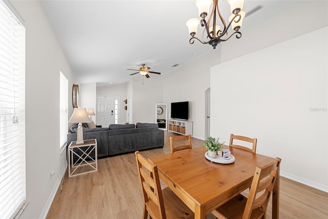 dining room with ceiling fan with notable chandelier, light wood-type flooring, and lofted ceiling