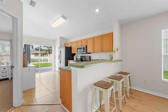 kitchen featuring black stove, kitchen peninsula, light wood-type flooring, lofted ceiling, and a kitchen bar