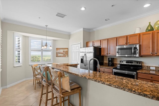 kitchen featuring light tile patterned floors, decorative light fixtures, appliances with stainless steel finishes, a breakfast bar area, and dark stone counters