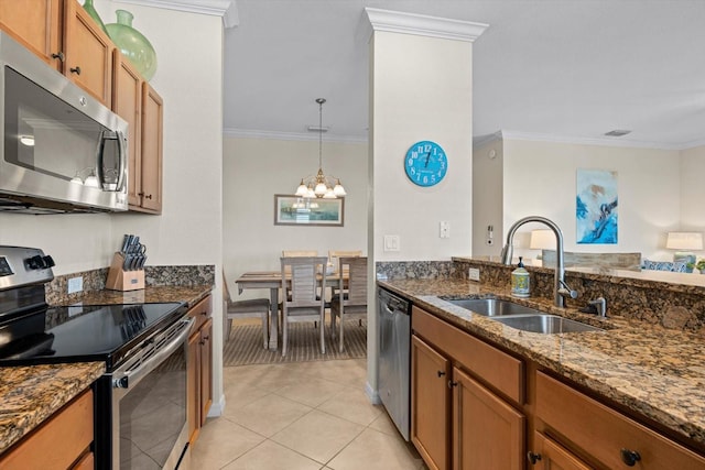 kitchen with ornamental molding, sink, stainless steel appliances, an inviting chandelier, and dark stone counters