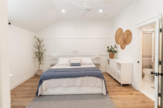 bedroom featuring light hardwood / wood-style floors, vaulted ceiling, ensuite bath, and ceiling fan