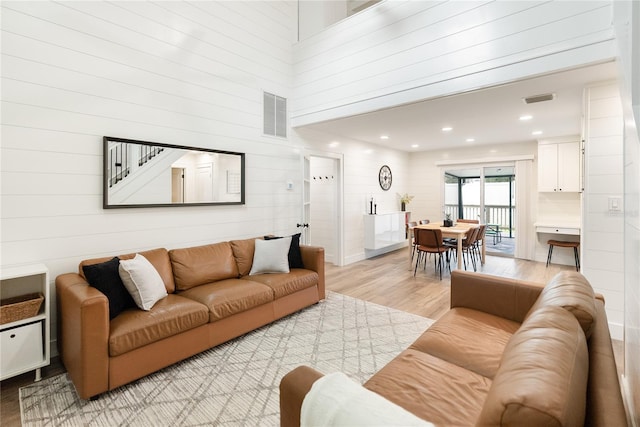 living room featuring light hardwood / wood-style flooring, a towering ceiling, and wood walls