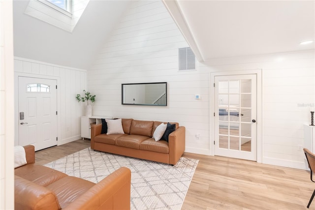 living room featuring a skylight, light hardwood / wood-style flooring, wooden walls, and high vaulted ceiling