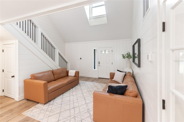 living room featuring high vaulted ceiling, wooden walls, light hardwood / wood-style floors, and a skylight