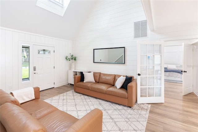 living room featuring high vaulted ceiling, wooden walls, a skylight, and light hardwood / wood-style flooring