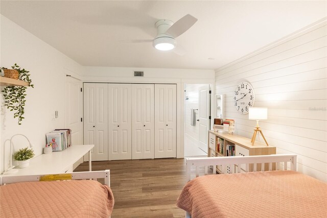 bedroom with ceiling fan, hardwood / wood-style flooring, a closet, and wooden walls