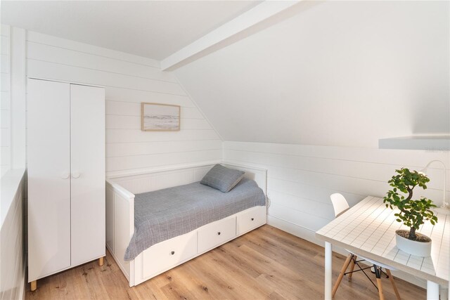 bedroom featuring wooden walls, light wood-type flooring, and vaulted ceiling