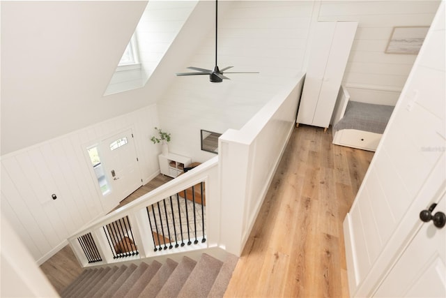 stairway featuring wood-type flooring, wooden walls, ceiling fan, and high vaulted ceiling