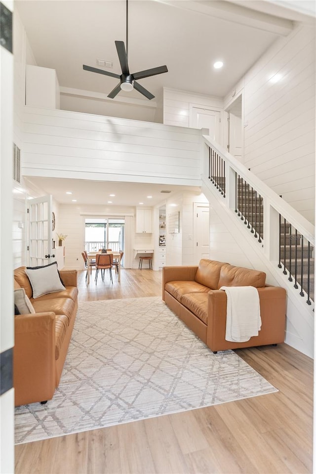 living room with ceiling fan, light hardwood / wood-style flooring, and a towering ceiling