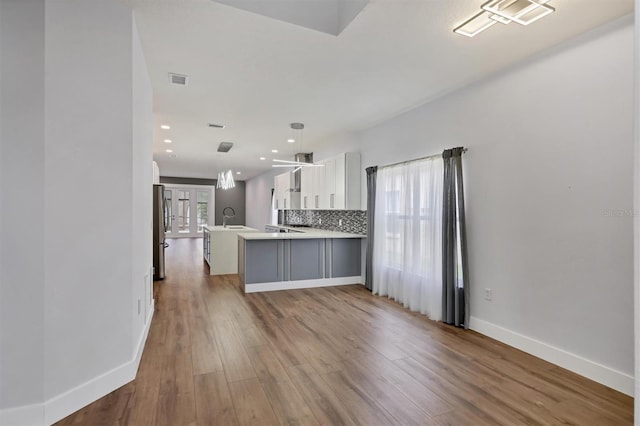 kitchen featuring white cabinets, kitchen peninsula, light wood-type flooring, and a healthy amount of sunlight