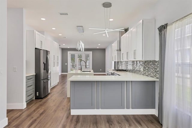 kitchen featuring white cabinetry, kitchen peninsula, decorative light fixtures, hardwood / wood-style flooring, and stainless steel refrigerator with ice dispenser