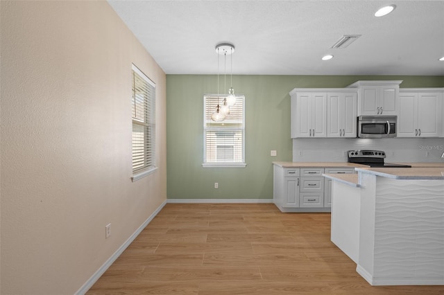 kitchen with white cabinets, stainless steel appliances, pendant lighting, and light hardwood / wood-style floors