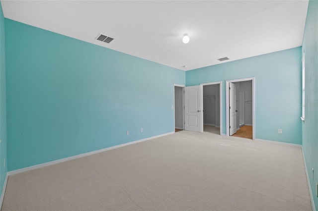 unfurnished bedroom with ensuite bathroom, light carpet, a walk in closet, and a closet