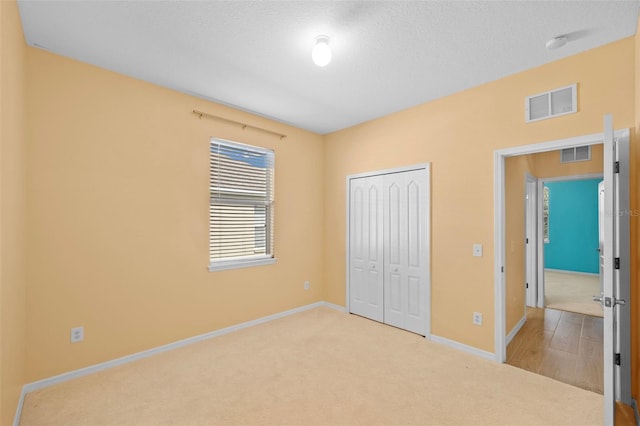 unfurnished bedroom with a closet, light colored carpet, and a textured ceiling