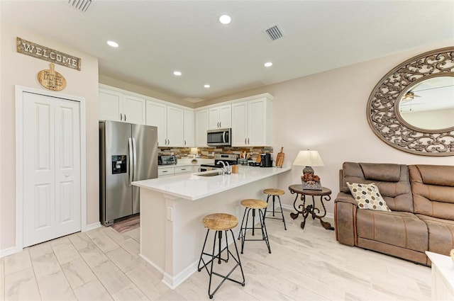 kitchen with appliances with stainless steel finishes, decorative backsplash, white cabinets, kitchen peninsula, and a breakfast bar area