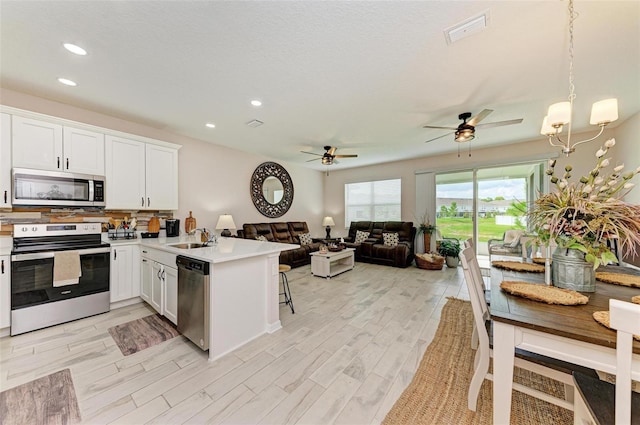 kitchen featuring hanging light fixtures, kitchen peninsula, white cabinetry, appliances with stainless steel finishes, and ceiling fan with notable chandelier