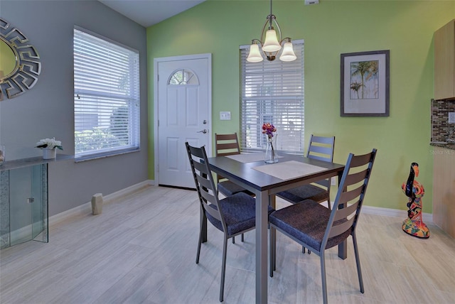 dining area with light wood-type flooring, a notable chandelier, and vaulted ceiling