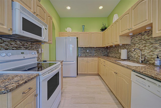 kitchen with light brown cabinetry, dark stone counters, white appliances, and sink