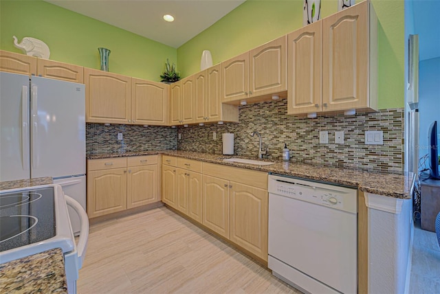 kitchen with decorative backsplash, dark stone countertops, sink, white dishwasher, and light brown cabinetry