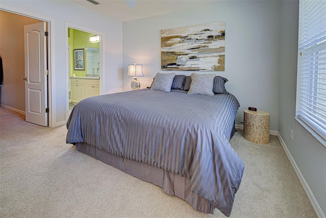 bedroom featuring ceiling fan, ensuite bath, and light colored carpet