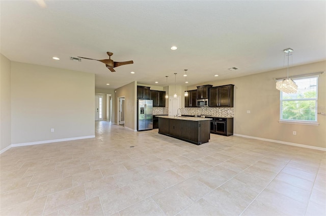 kitchen featuring decorative backsplash, an island with sink, stainless steel appliances, pendant lighting, and ceiling fan with notable chandelier